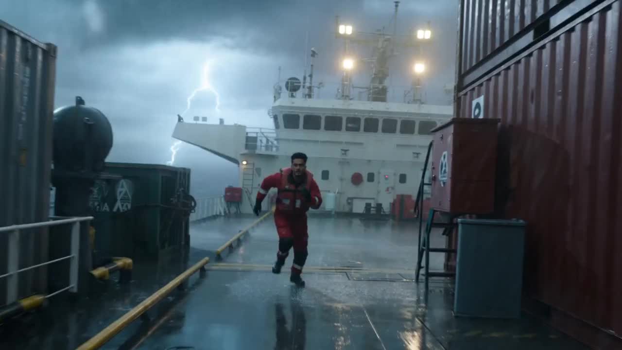 A man (reference image @image1  ) dressed in a red rescue suit, runs along the deck of a huge cargo 