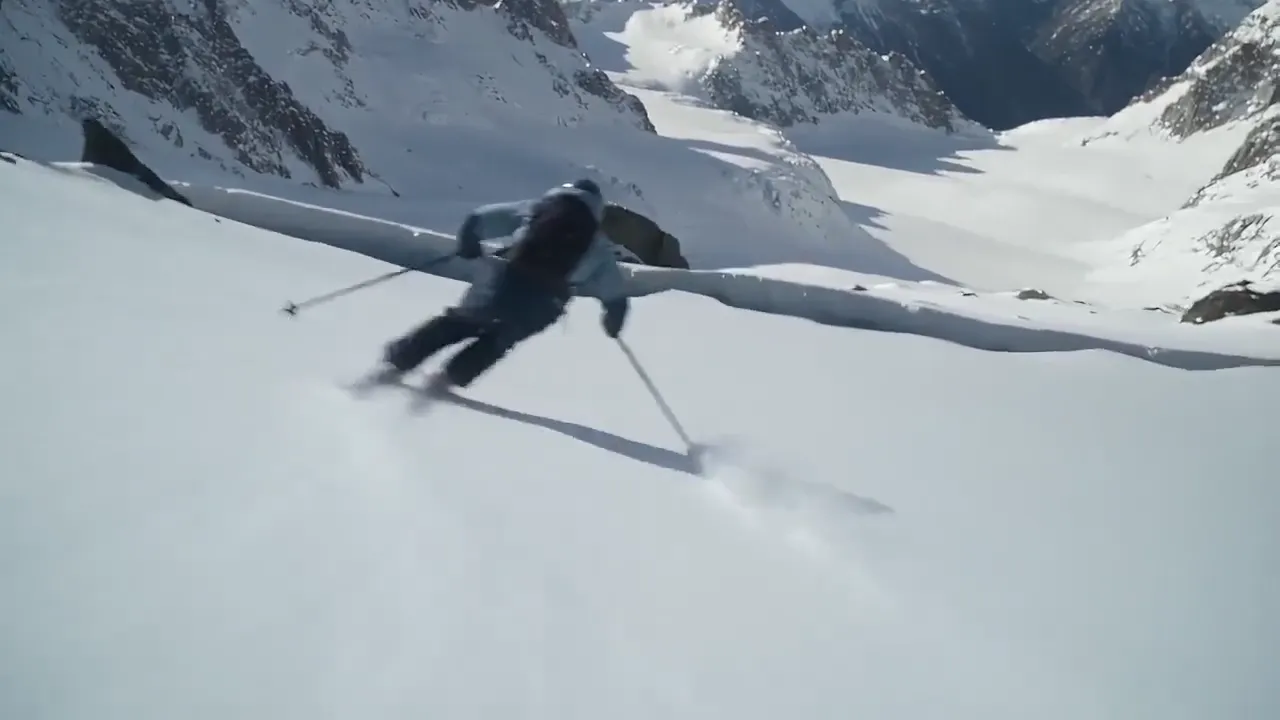 A skier in a grey jacket and goggles racing down a snowy mountain