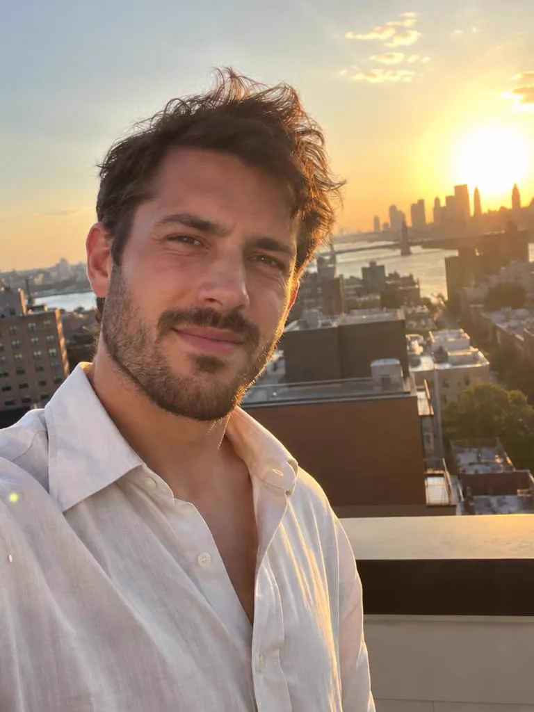 Take 2: the same rooftop sunset selfie after a retake, his eyes open and a relaxed smile